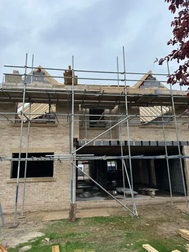 Two-storey extension shell and twin gables under construction with scaffolding.