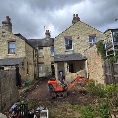 Rear elevation of a yellow gault brick Victorian house in Cambridge with a mini excavator in the garden at the start of the works