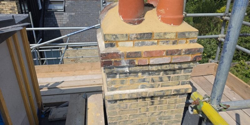 Rebuilt yellow gault brick chimney stack with clay pots above a Cambridge terrace, scaffolded
