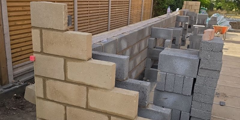 Corner of new blockwork built on a blue engineering brick plinth above the damp-proof course, with the first lift of the extension walls behind, Great Shelford