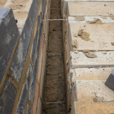 Close-up of the cavity between the engineering brick outer leaf and the block inner leaf, with wall ties and the damp-proof course, beside the beam-and-block floor
