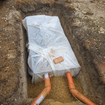 Modular soakaway crate wrapped in geotextile membrane set in an excavated pit with two surface water pipes connected, Great Shelford