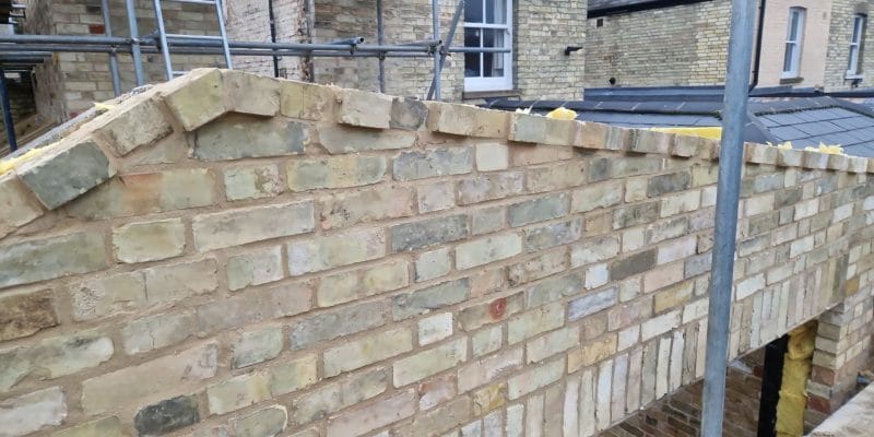 New yellow gault brick parapet finished with a raking brick-on-edge coping that follows the roof pitch
