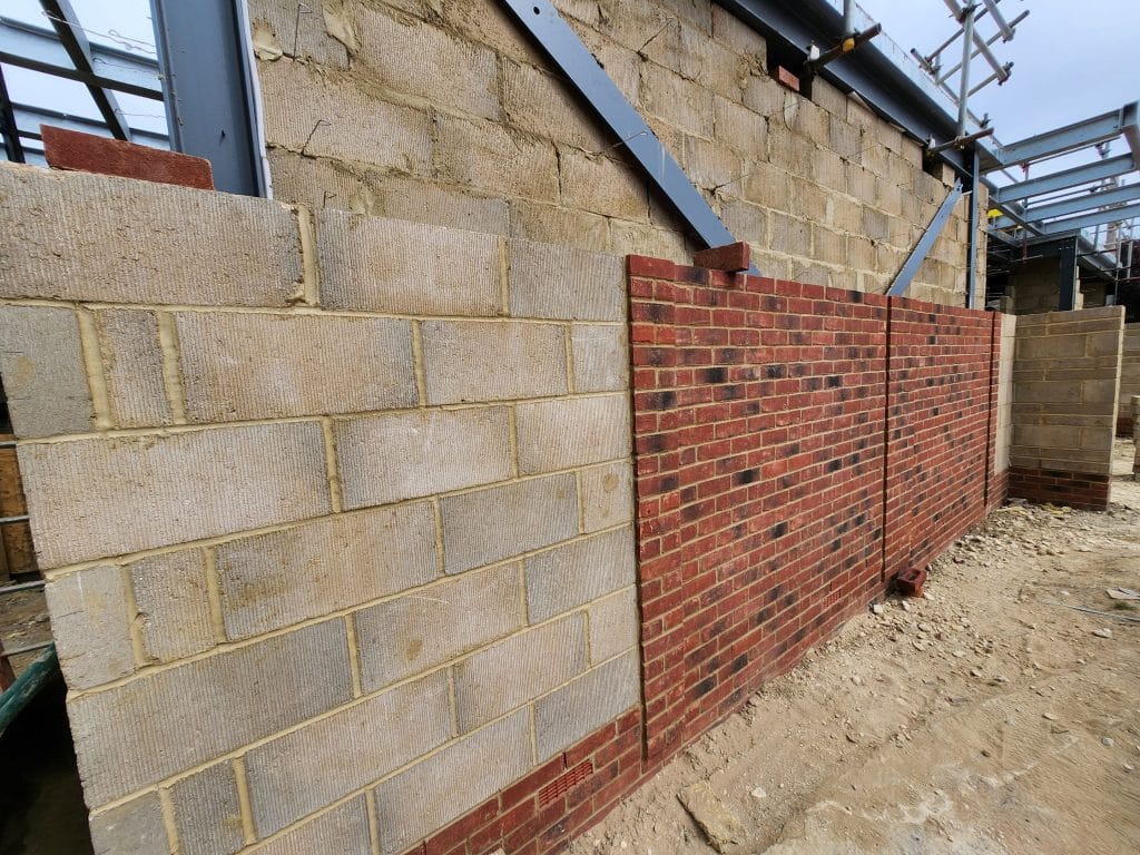 Cavity wall under construction with a blockwork inner leaf on the left and a red facing brick outer leaf on the right
