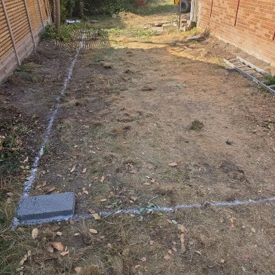 The footprint of a new extension set out in chalk lines across stripped ground between the boundary fence and the existing brick house wall