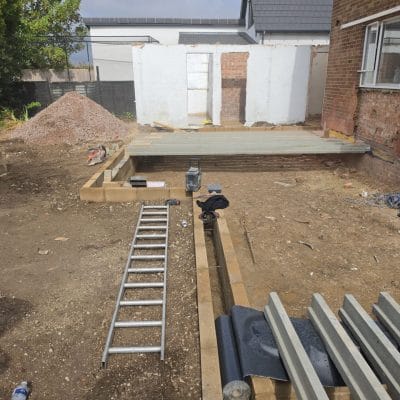 Blockwork foundation walls built up to damp-proof course forming the extension room layout, with the first bay of precast concrete floor beams laid