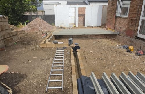 Blockwork foundation walls built up to damp-proof course forming the extension room layout, with the first bay of precast concrete floor beams laid