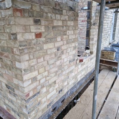 New yellow gault brick quoin showing stretcher bond on both returns, a dark cavity tray course and open perpend weep vents along its base