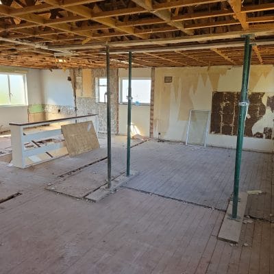 A stripped ground-floor room with the ceiling plasterboard removed to expose the timber joists and three adjustable steel props supporting them