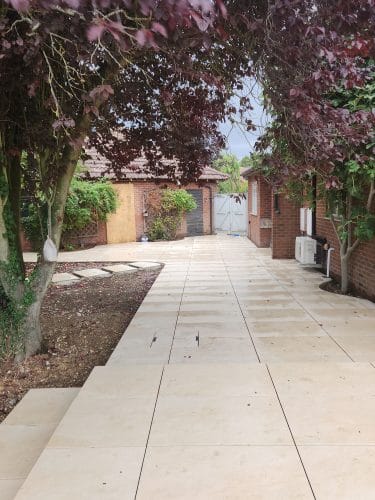 Porcelain paving running along the side of the house towards the garden gates, under a purple-leaved tree, Bar Hill